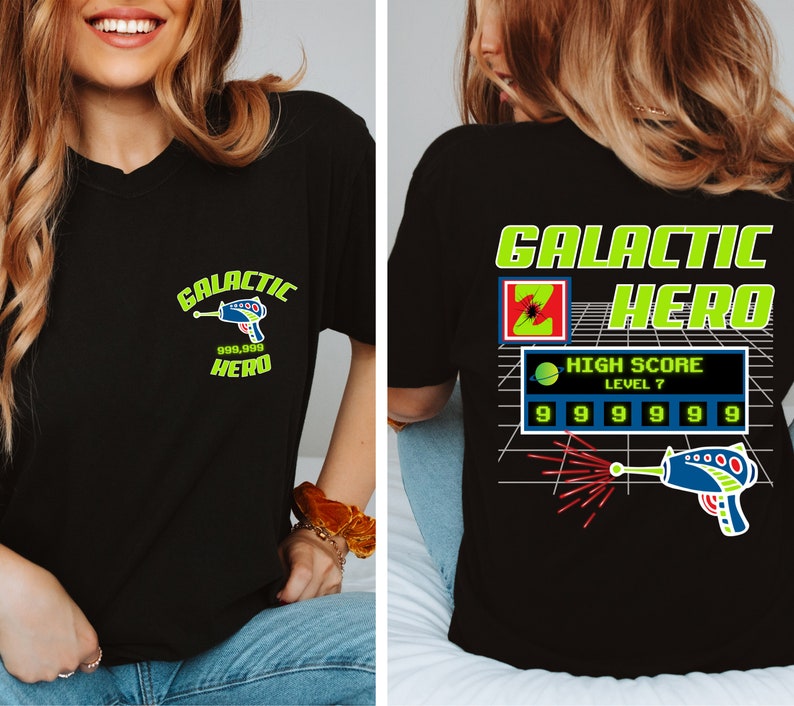May include: Black t-shirt with a green and yellow graphic design that says "Galactic Hero" and features a pixelated spaceship and a high score of 999,999. The graphic also includes the text "High Score Level 7".