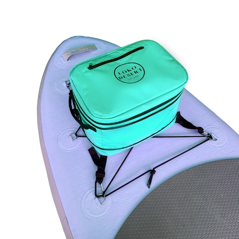 May include: A turquoise cooler bag with black straps and the text "LOKO DESERT" in a circle on the front. The bag is attached to a white inflatable paddleboard with black straps.