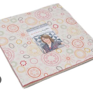 May include: A stack of fabric squares with a white background and a repeating pattern of colorful circles and stars. The fabric squares are labeled "moda" and "designed by Amy Butler".