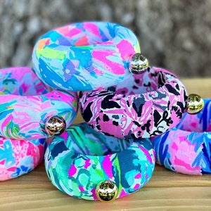 May include: A stack of five colourful fabric bangles with gold-toned accents. Each bangle features a different floral print.