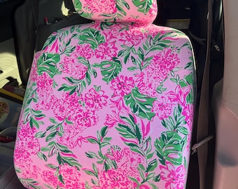Op de afbeelding: Roze autostoelbekleding met een bloemenpatroon in roze en groene tinten. Het ontwerp toont grote bloemen en bladeren op een lichtroze achtergrond. De stoelbekleding is in een voertuig geïnstalleerd.