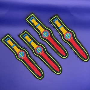 May include: Four embroidered patches in the shape of wristwatches. Each patch features a red watch strap, a yellow buckle, and a blue and green watch face. The patches are outlined in black with a neon green border, set against a blue background.