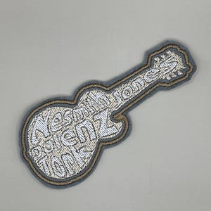 May include: Embroidered guitar-shaped patch with the text "Yes I'm a Totem Tool" in white thread. The patch has a gray border with a tan outline, set against a light gray background. Ideal for jackets, bags, or other fabric items.