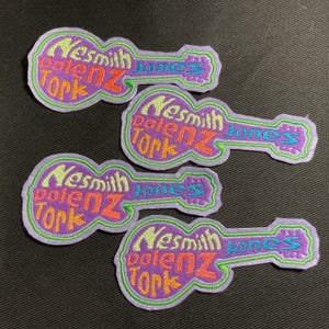 May include: Four embroidered patches in the shape of a guitar. Each patch features the words "Nesmith Jones Tork" in various colors, including orange, green, and blue, on a purple background. The patches have a green border.