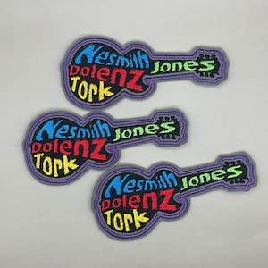 May include: Three embroidered patches in the shape of a guitar. Each patch features the words "Nesmith", "Dolenz", "Tork", and "Jones" in a colorful, stylized font. The patches have a gray border.