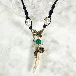 May include: A black leather cord necklace with two white skull beads, a bronze butterfly charm, a green malachite bead, and a white antler pendant with a bronze rose.