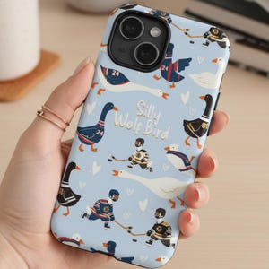 May include: A light blue phone case featuring a whimsical design with geese, hockey players, and the text "Silly Wolf Bird." The case has a repeating pattern of the illustrated elements. The phone case is held in a hand.