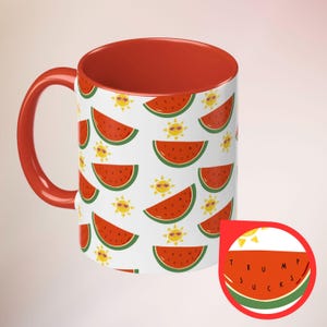 May include: A white ceramic mug with a red interior and handle. The mug features a pattern of watermelon slices and smiling suns. A small watermelon-shaped sticker with the text "TRUMP SUCKS" is also visible.