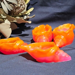 May include: Four small, orange and pink seashell-shaped bowls. The bowls are made of a smooth, glossy material and have a slightly iridescent finish.