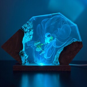May include: A unique, illuminated resin art piece featuring a blue astronaut figure within a glowing, geometric design. The artwork is set on a wooden base, creating a striking contrast between the natural wood and the futuristic resin.