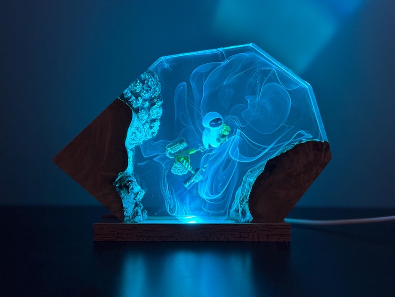 May include: A unique, illuminated resin art piece featuring a blue astronaut figure within a glowing, geometric design. The artwork is set on a wooden base, creating a striking contrast between the natural wood and the futuristic resin.
