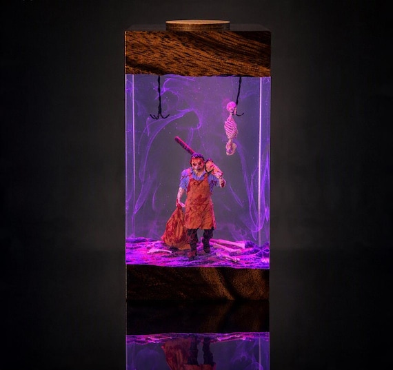 A hand-poured epoxy resin lamp trapping a slasher horror scene inside glowing wood — equal parts nightlight and collector's art piece.