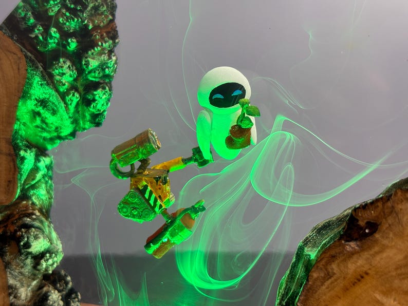 May include: A whimsical artwork featuring the characters Wall-E and Eve from the animated film. Eve, in a glowing green hue, holds a plant. Wall-E, with yellow and green accents, is also present. The background has green swirls.