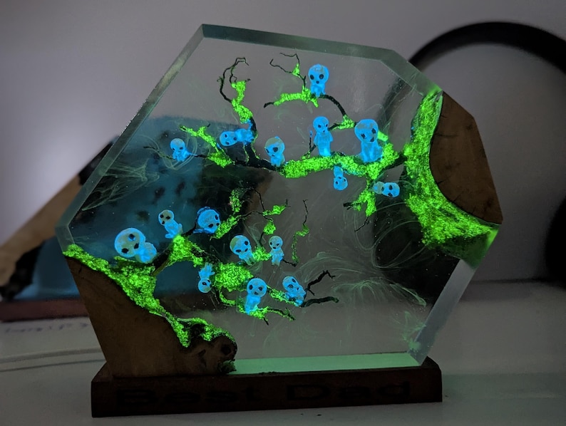 Pu&ograve; includere: Una scultura esagonale in resina con un albero verde luminoso e figure blu luminose. La scultura &egrave; su una base di legno.