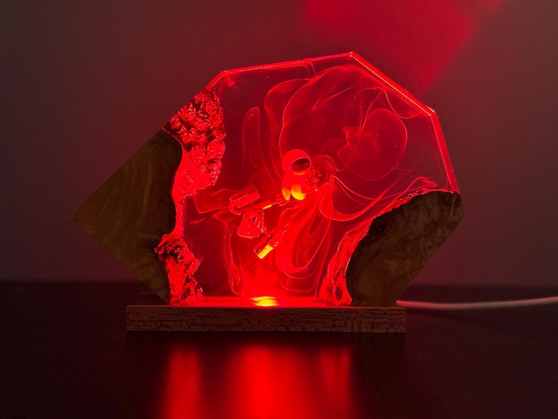 May include: A unique, geometric-shaped lamp with a red glow. The lamp features a clear, resin-like center with an abstract design, framed by natural wood elements. The base is a rectangular wooden platform.