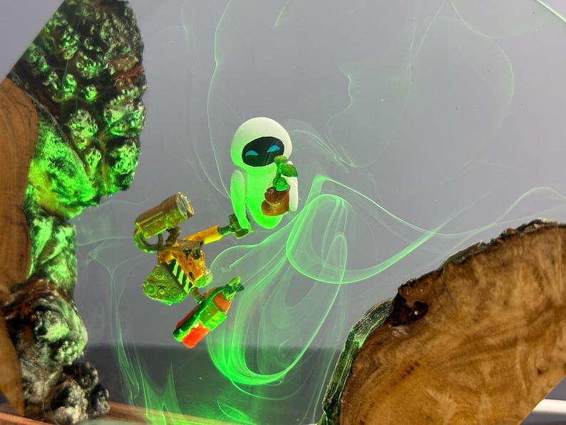 May include: A whimsical artwork featuring the animated characters Wall-E and Eve. Eve is depicted in a glowing green hue, holding a small object. Wall-E is shown with a yellow and orange body, holding a bottle. The background has green swirls and wooden accents.