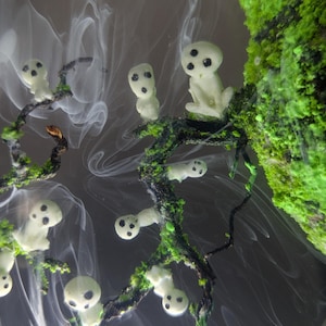 Pu&ograve; includere: Figurini in resina bianca con occhi neri, che ricordano gli spiriti, sono disposti su un ramo con muschio verde. I figurini sono circondati da vortici bianchi simili a fumo.