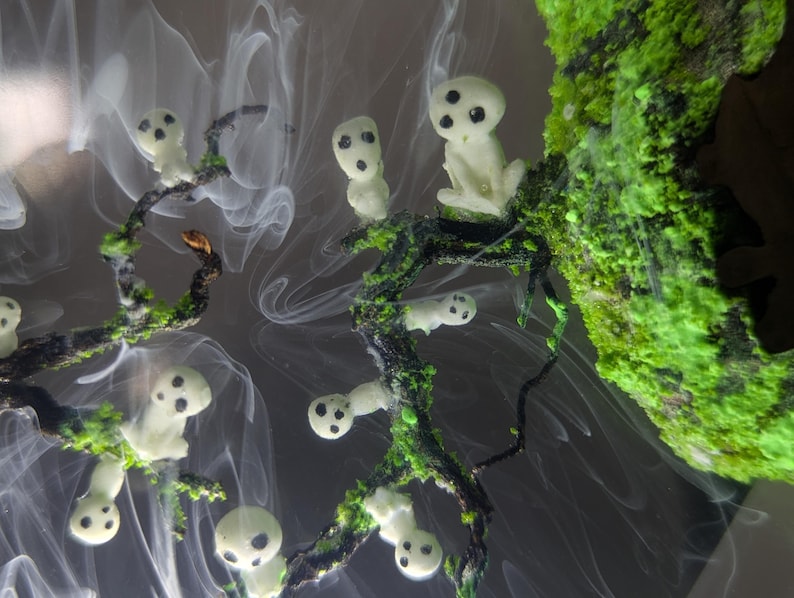 Pu&ograve; includere: Figurini in resina bianca con occhi neri, che ricordano gli spiriti, sono disposti su un ramo con muschio verde. I figurini sono circondati da vortici bianchi simili a fumo.
