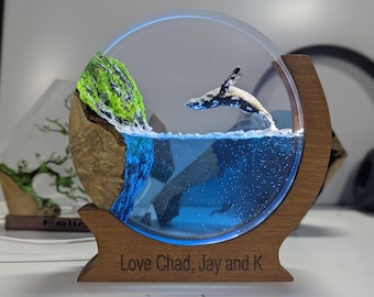May include: A whale sculpture leaping out of a blue resin ocean inside a clear round dome. The dome is mounted on a wooden base with the inscription "Love Chad, Jay and K".