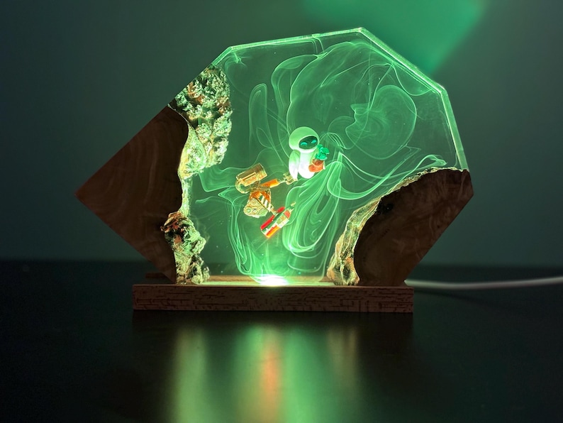 May include: A unique, illuminated resin lamp featuring a geometric design. The lamp showcases a small astronaut figure and a robot within a glowing green resin. The base is made of wood, and the lamp emits a soft, ambient light.