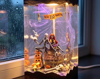 May include: A rectangular Halloween-themed lamp featuring Jack Skellington and Sally from The Nightmare Before Christmas. The lamp has a wooden base and a clear acrylic enclosure with a "HALLOWEEN" banner. Inside are pumpkins, a skull, and purple smoke.