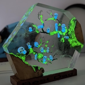 Pu&ograve; includere: Una scultura in resina trasparente con un albero verde fluorescente e teschi blu. La scultura &egrave; su una base di legno.