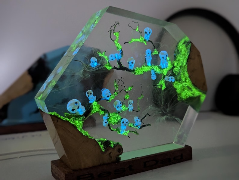 Pu&ograve; includere: Una scultura in resina trasparente con un albero verde fluorescente e teschi blu. La scultura &egrave; su una base di legno.