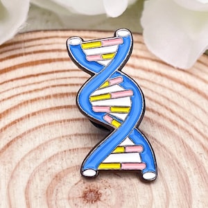 May include: A blue, yellow, and pink enamel pin in the shape of a DNA double helix. The pin has a white border and is set against a wooden background. The design is a representation of the structure of DNA.