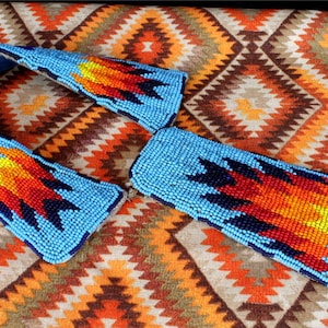 May include: A beaded Native American choker necklace with a blue background and orange, red, and yellow flame designs. The necklace is made of small, colorful beads and is laid out on a patterned fabric.
