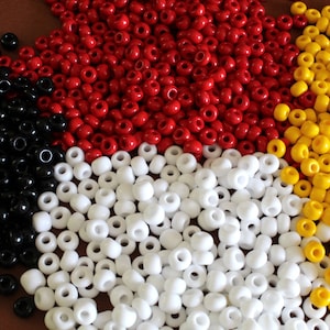 Puede incluir: Una colección de pequeñas cuentas redondas en varios colores: negro, rojo, blanco y amarillo. Las cuentas están dispersas sobre una superficie, creando una disposición visualmente atractiva. Adecuado para la fabricación de joyas y proyectos de artesanía.