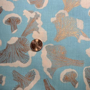 以下が含まれることがあります： 白と金のキノコ模様の青い布。キノコはスタイリッシュで、繊細でレースのような外観をしています。