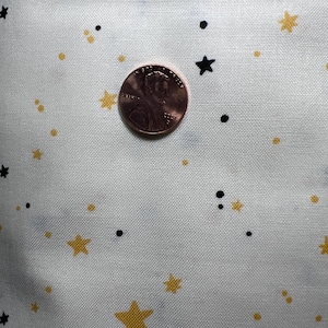 May include: White fabric with a repeating pattern of small gold stars and black dots. A US penny is placed on the fabric for scale.