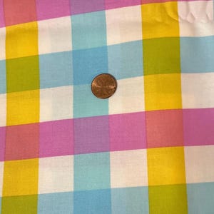 Peut inclure: Gros plan sur un tissu à motif vichy coloré. Le motif présente des carrés jaunes, roses, violets, bleus, verts et blancs. Une pièce de monnaie est placée sur le tissu pour l'échelle.