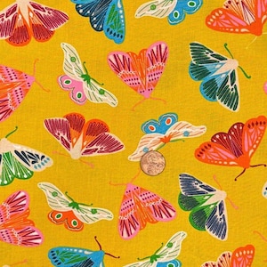 Puede incluir: Una tela de color amarillo mostaza con un patrón repetitivo de polillas estilizadas en varios colores, incluyendo azul, rosa, naranja y verde. Una moneda de color cobre está colocada sobre la tela para dar una escala de las ilustraciones.