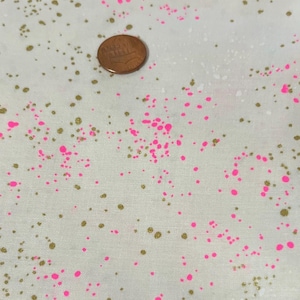 Puede incluir: Primer plano de una tela con un patrón moteado. La tela es blanquecina con salpicaduras de pintura doradas y rosas. Una moneda de cobre está sobre la tela para la escala. La tela probablemente se utiliza para proyectos de artesanía o costura.