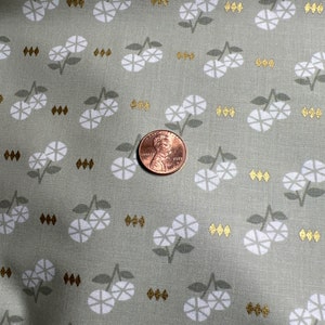 Puede incluir: Primer plano de una tela verde con un patrón floral blanco y detalles dorados. Un centavo estadounidense se coloca sobre la tela para la escala.