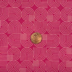 Puede incluir: Tela rosa intenso con un patrón geométrico repetitivo de arcos y círculos entrelazados en rosa claro. Se incluye una moneda para la escala. El diseño tiene un ambiente retro de los años 70.