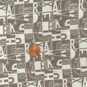 May include: Close-up of a fabric with a repeating pattern of letters and geometric shapes in white and brown. A penny is placed on the fabric for scale. The design includes the letters A, Z, E, K, and R.