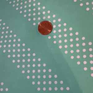 May include: A close-up of a turquoise fabric with a white polka dot pattern. A copper penny is placed on the fabric.