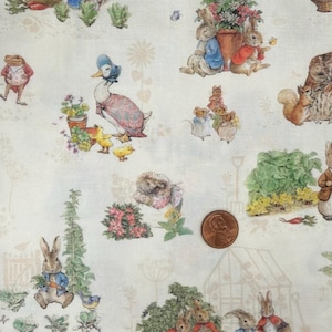 May include: A light-colored fabric featuring a repeating pattern of Beatrix Potter characters including Peter Rabbit, Jemima Puddle-Duck, and an owl, alongside garden elements like flowers and vegetables, with a copper penny for scale.