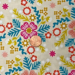 Puede incluir: Primer plano de una tela floral con fondo crema. El diseño presenta flores y hojas rosas, naranjas, amarillas y turquesas. Se incluye una moneda para la escala. La tela tiene un patrón repetido de flores y follaje estilizados.