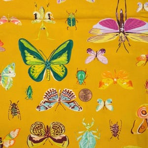 May include: Mustard yellow fabric with a repeating pattern of colorful butterflies and insects. The insects are in various sizes and shapes, with details in green, blue, pink, and orange. A penny is visible in the center of the image.