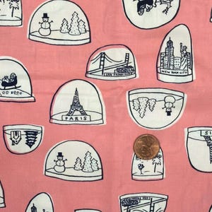 Puede incluir: Una tela rosa con un patrón repetitivo de bolas de nieve dibujadas con líneas negras y blancas que representan varios monumentos y escenas navideñas, incluyendo París, Nueva York y San Francisco, con una moneda de cobre sobre una bola.