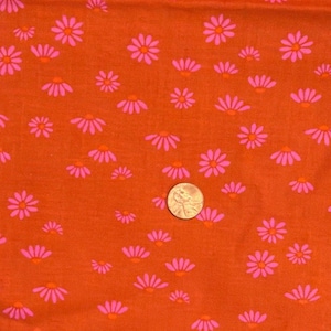 May include: Close-up of orange fabric with a repeating pattern of pink and orange daisy-like flowers. A coin is included for scale. The fabric has a soft, textured appearance, and the floral design is evenly distributed across the surface.