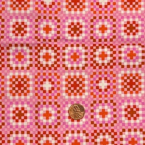 Peut inclure: Tissu rose avec un motif répétitif de carrés et de croix dans des tons orange, rouge et blanc. Une pièce de monnaie est placée sur le tissu pour l'échelle. Le tissu a un design rétro et géométrique.