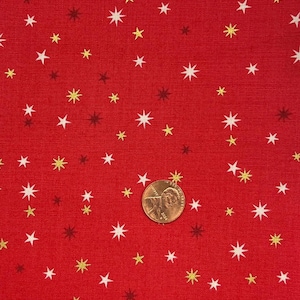 May include: Red fabric featuring a repeating pattern of white, gold, and brown stars. A penny is included for scale. The fabric has a textured appearance.