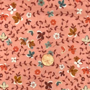 May include: Close-up of a floral fabric with a peach background. The fabric features a repeating pattern of small flowers in white, orange, brown, and teal, connected by brown vines. A penny is visible in the center of the fabric.