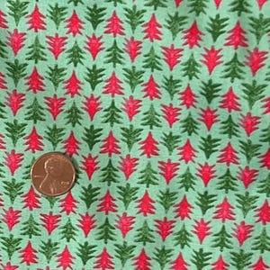 Puede incluir: Primer plano de una tela con un patrón repetido de árboles de Navidad. Los árboles alternan entre rojo y verde, sobre un fondo verde claro. Una moneda está en la esquina inferior izquierda para la escala.