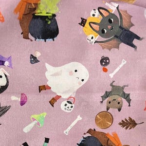 May include: A light purple fabric featuring Halloween-themed illustrations. The design includes a cartoon bear stirring a cauldron, a ghost with a trick-or-treat bucket, bats, mushrooms, and bones. The fabric is covered in various Halloween-themed images.