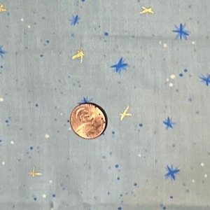 May include: A light blue fabric featuring a pattern of small blue and gold stars and white dots. A copper penny is placed on the fabric to provide a sense of scale, measuring approximately 0.75 inches in diameter for reference.